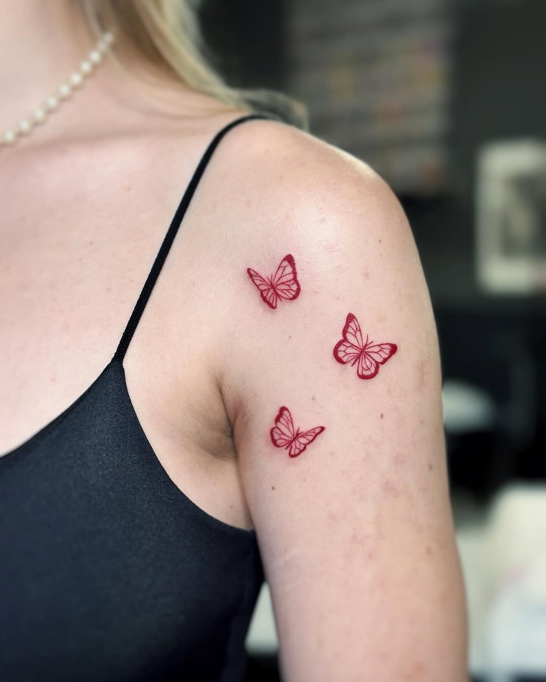 This image features three intricately designed red butterfly tattoos, delicately placed on a woman's shoulder.