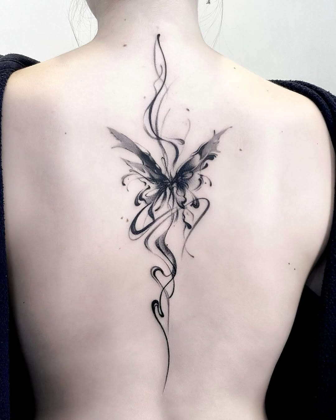 This stunning butterfly tattoo, inked in black, elegantly spans the back with delicate swirls.