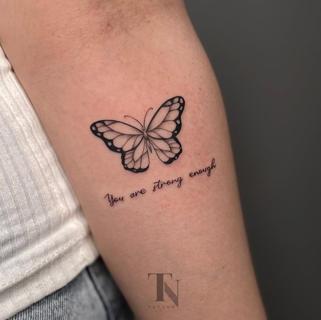 This tattoo features a beautifully intricate butterfly outlined in black ink, symbolizing transformation and resilience.