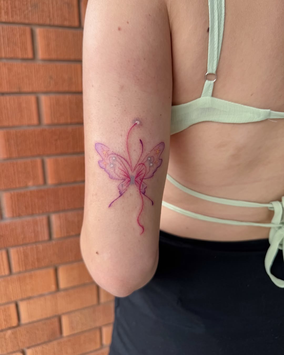 This tattoo showcases a beautifully crafted butterfly with soft pink hues and intricate designs.