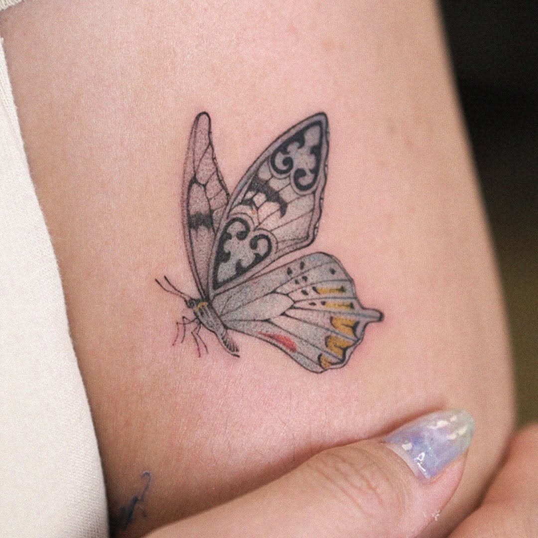 This tattoo features a delicate butterfly with gray shades and intricate designs.