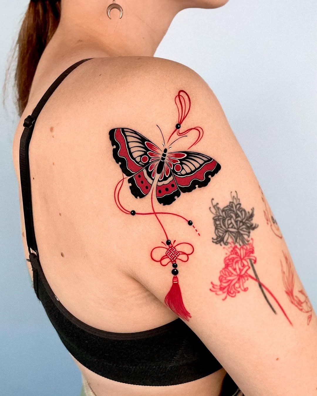 This butterfly tattoo features bold red and black colors, showing intricate linework and playful decorative elements.