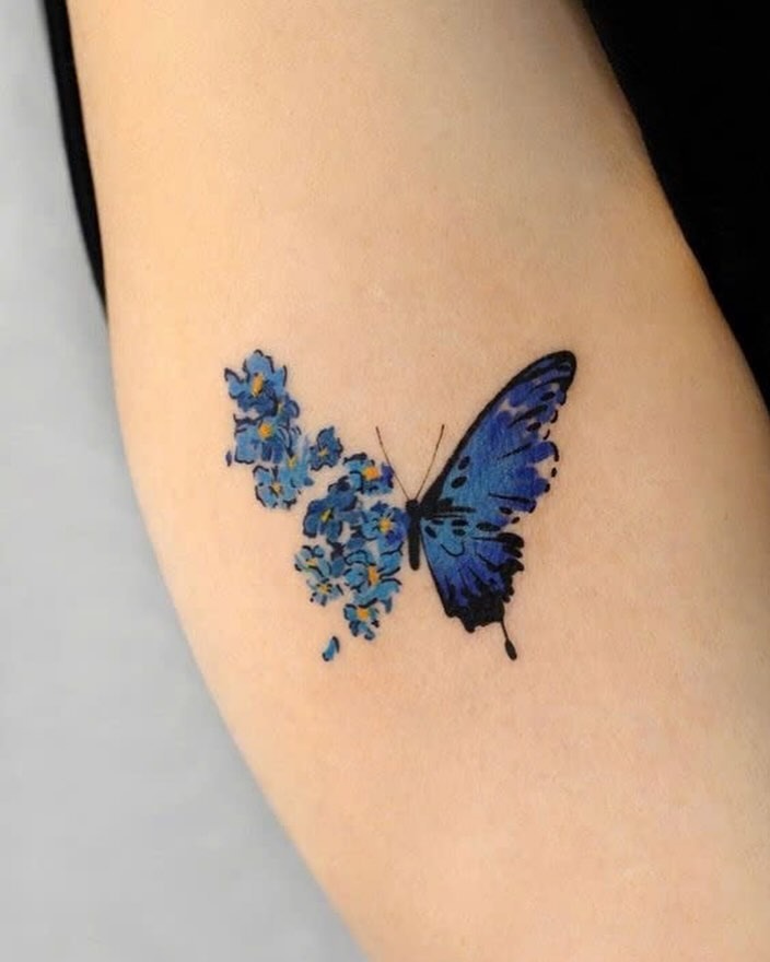 This butterfly tattoo features stunning blue hues alongside delicate floral elements.