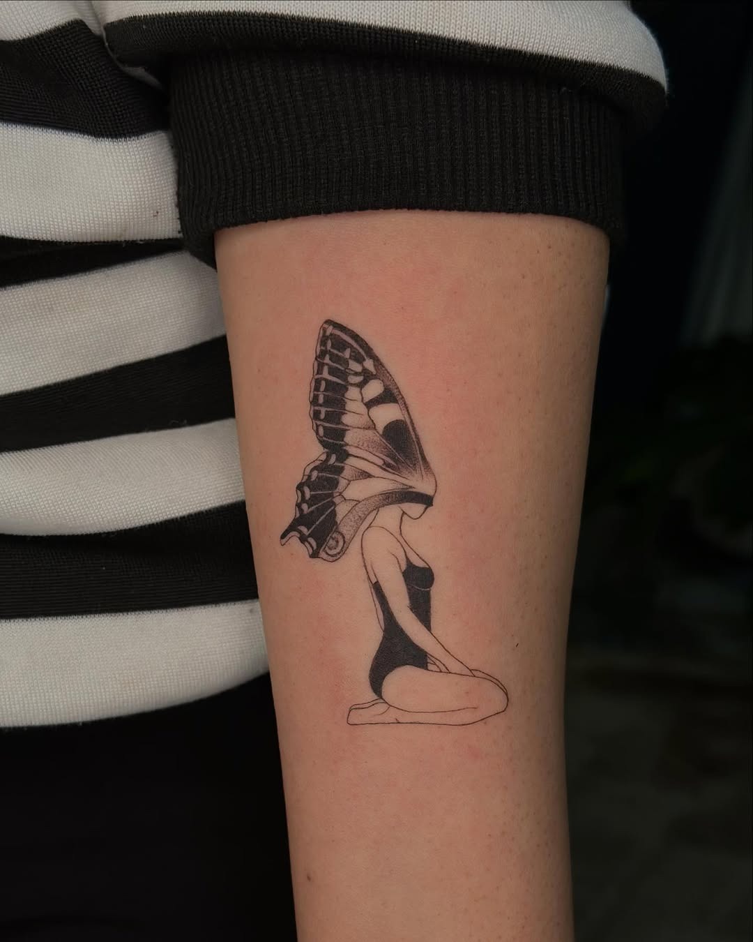 This striking tattoo features a silhouette of a woman with a butterfly emerging from her head.