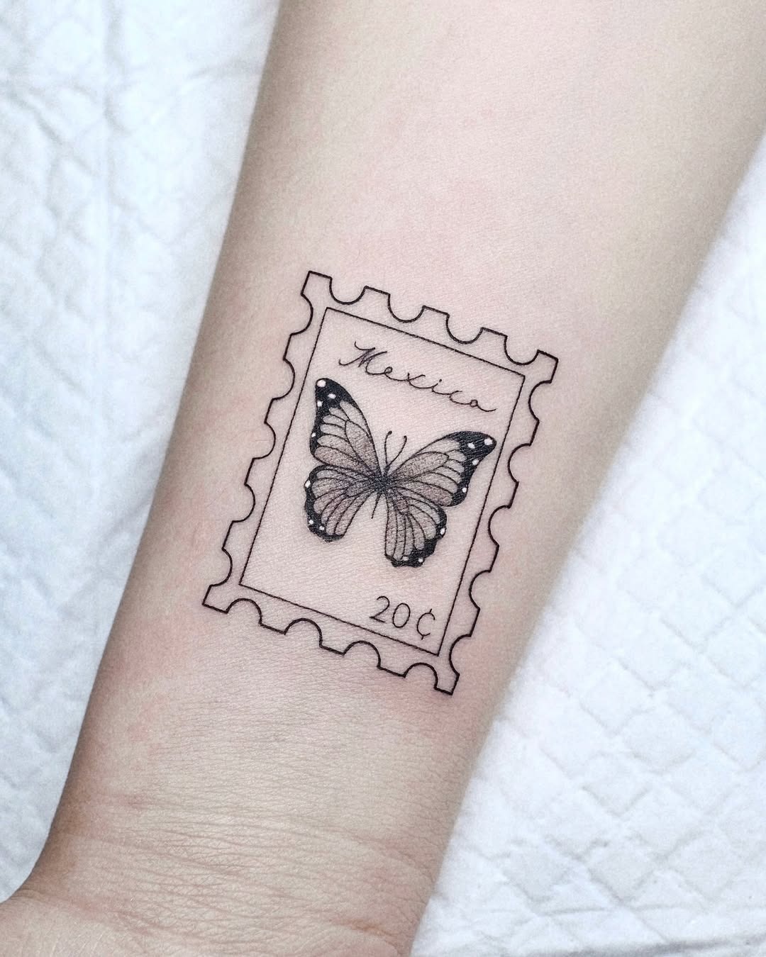 This tattoo features a beautifully detailed butterfly inside a vintage stamp design.