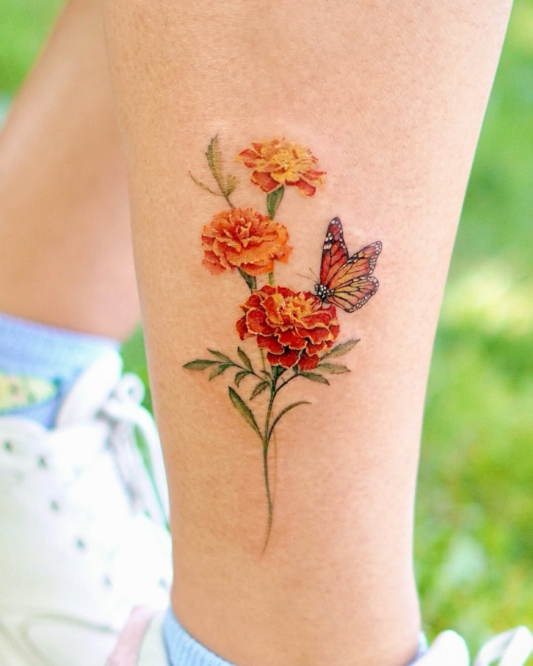 This tattoo features a stunning butterfly perched delicately on marigold flowers.
