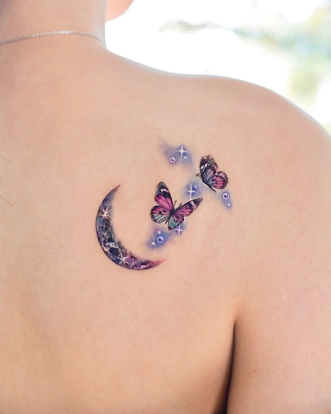 This tattoo features delicate butterflies fluttering around a dreamy crescent moon.