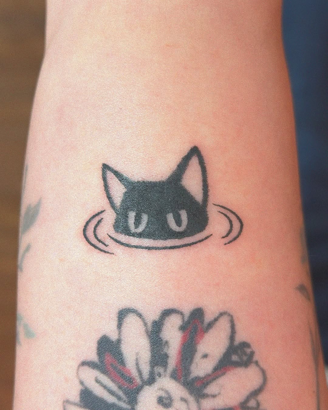 Charming black cat peeking above water Tattoo Design