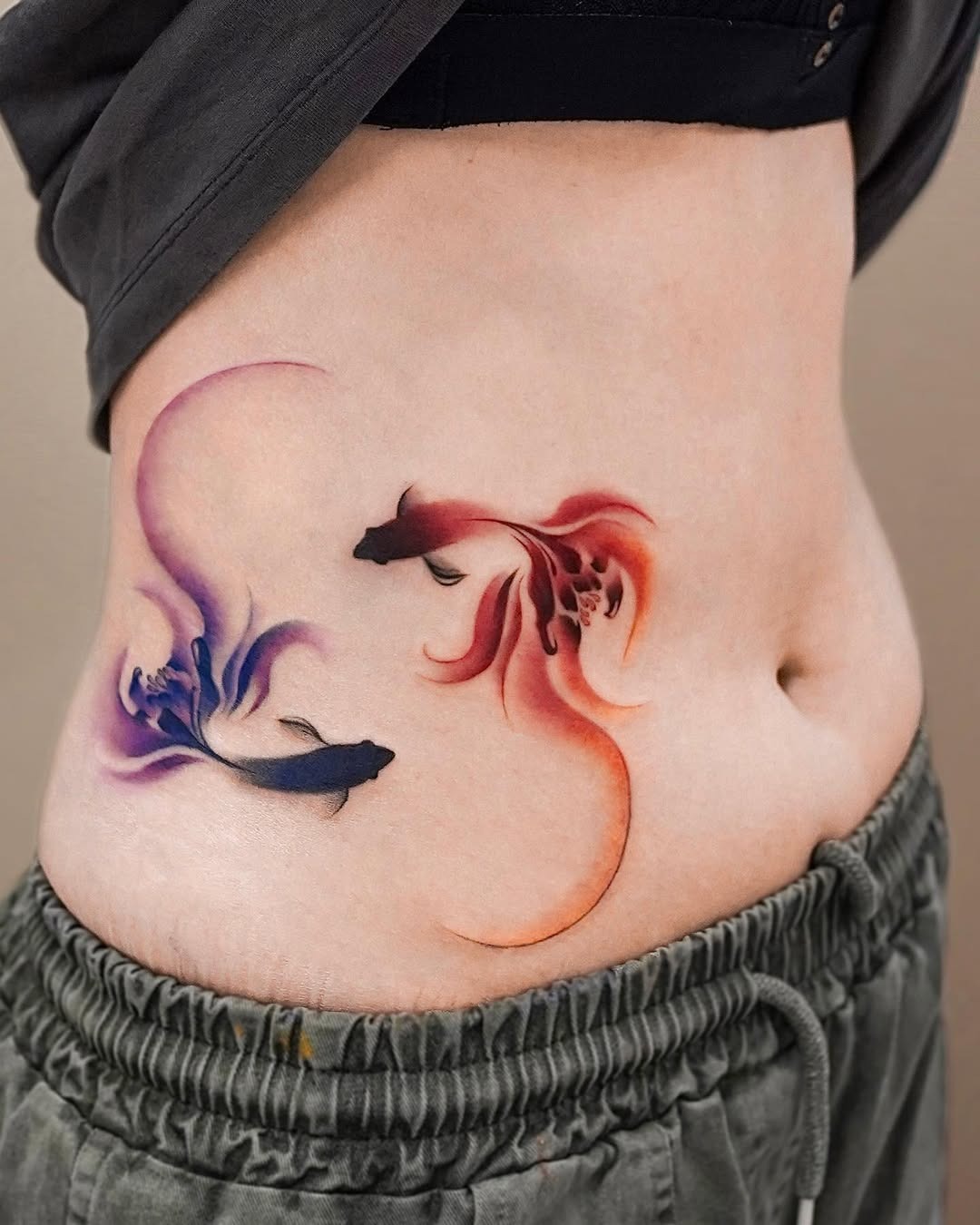 This tattoo showcases two koi fish in a swirling pattern, blending purple and red hues.
