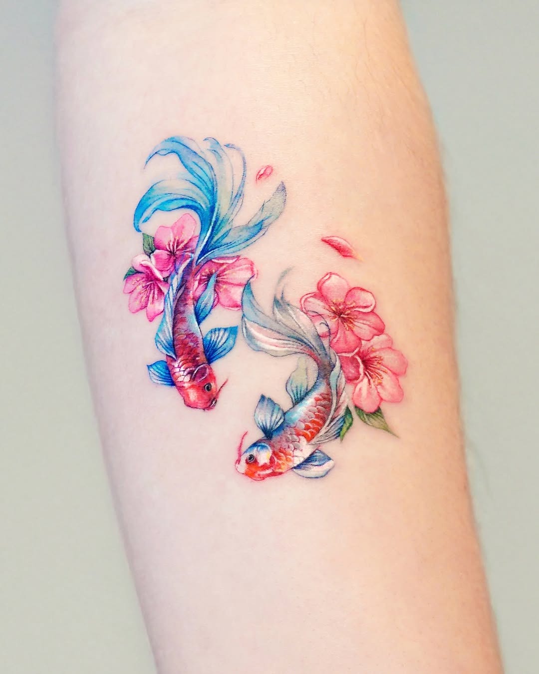 This tattoo features two koi fish swimming among pink flowers.