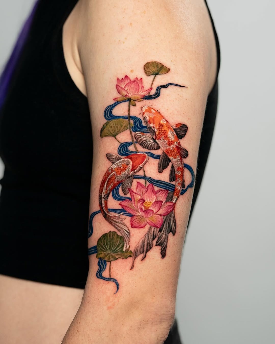 This striking koi fish tattoo features two beautifully detailed fish entwined with pink lotus flowers.
