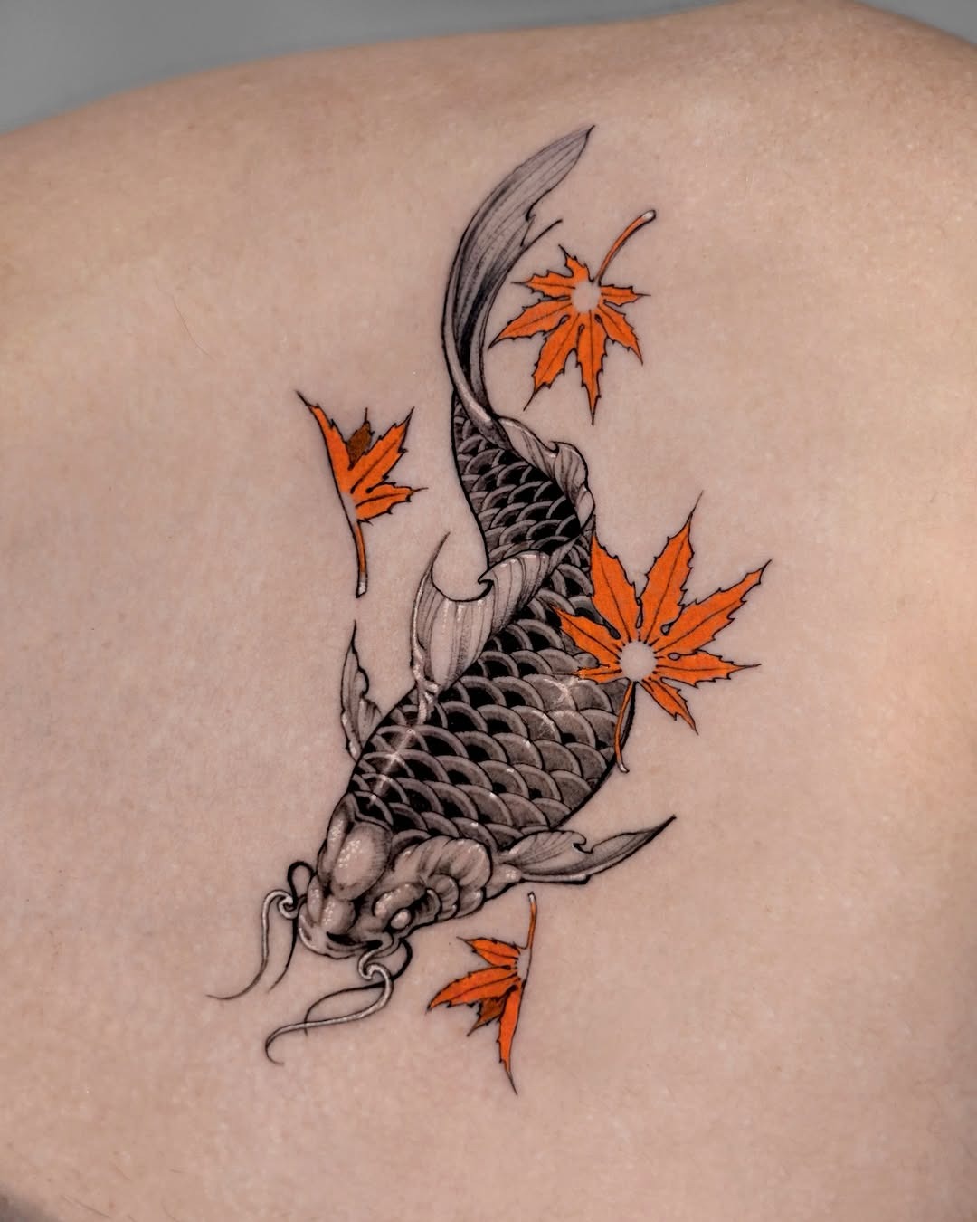 This tattoo features a beautifully detailed koi fish swimming gracefully, surrounded by orange maple leaves.