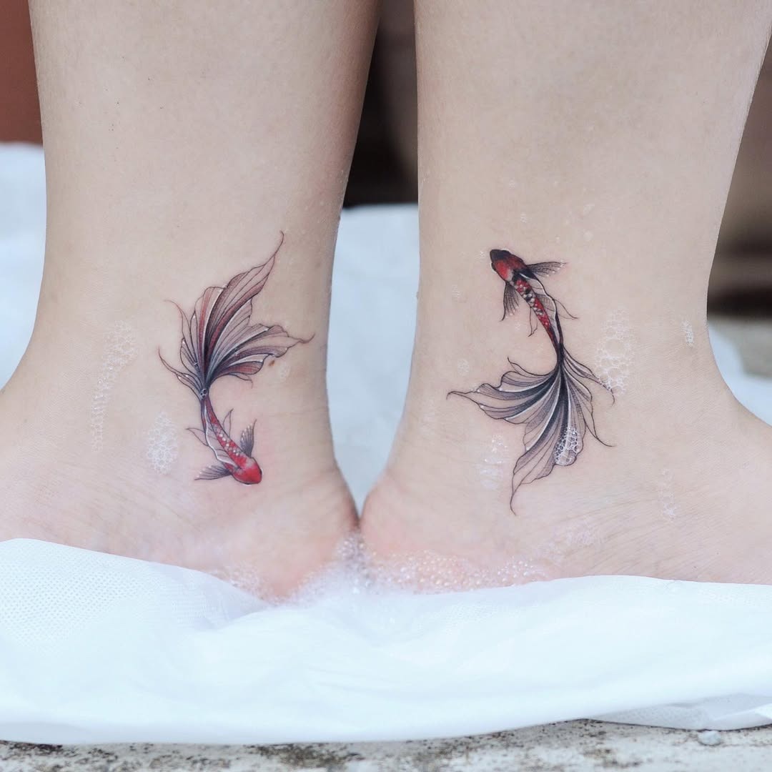 This tattoo features two beautifully detailed koi fish gracefully swimming around the ankle area.