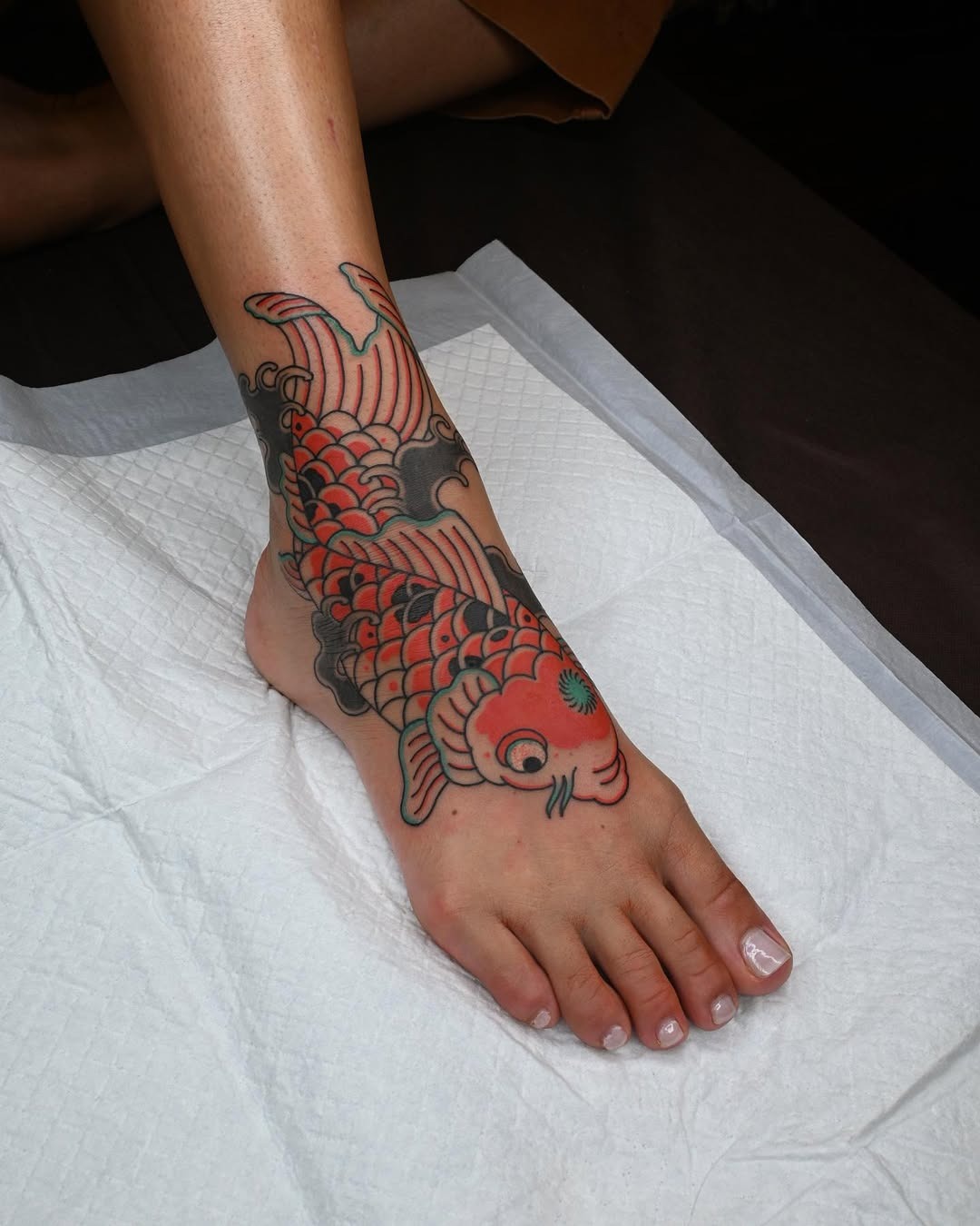 This koi fish tattoo elegantly wraps around the ankle, showing intricate details and bold colors.
