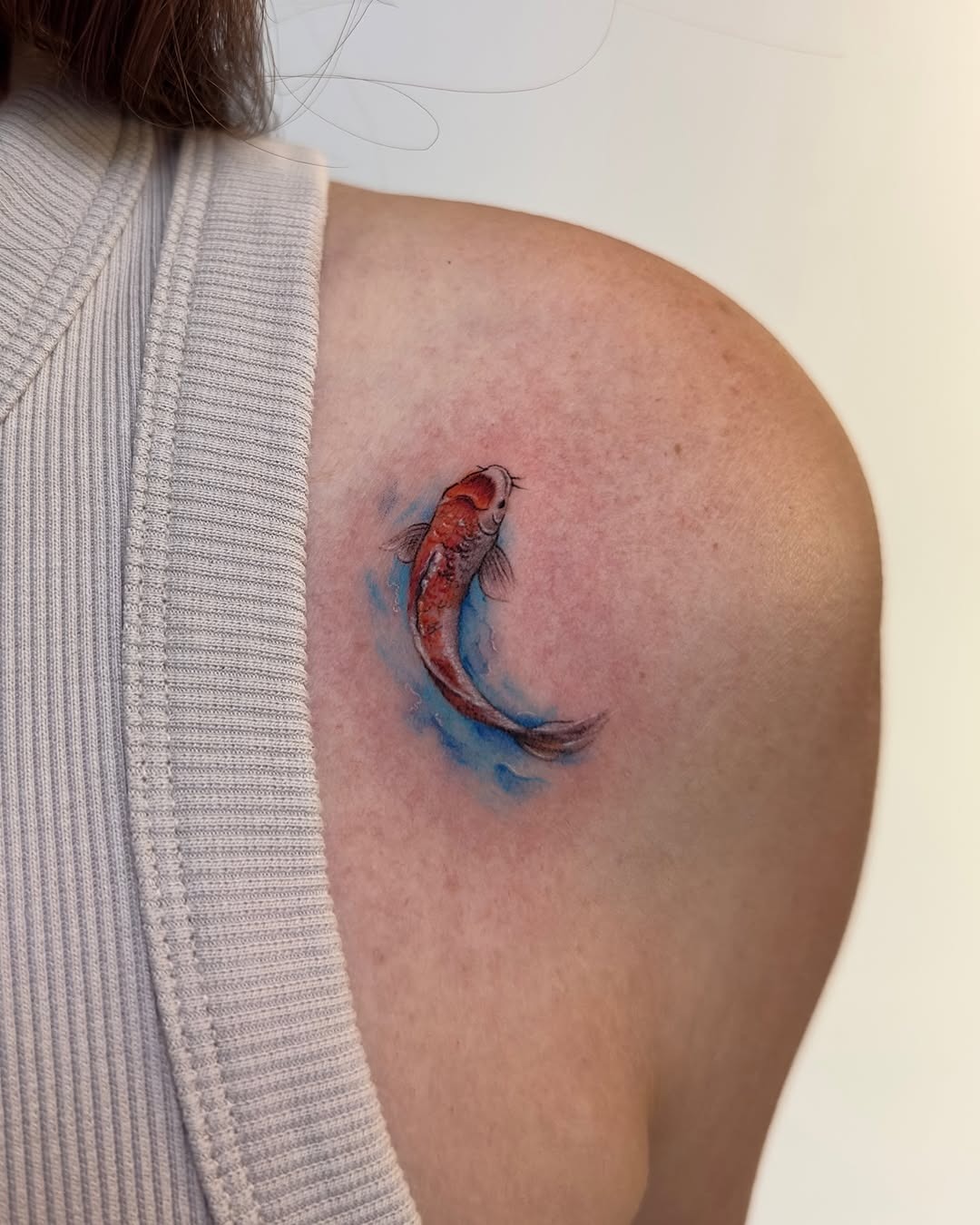 This koi fish tattoo brings a burst of color to the skin, showing a lively red fish gracefully swimming through splashes of blue.