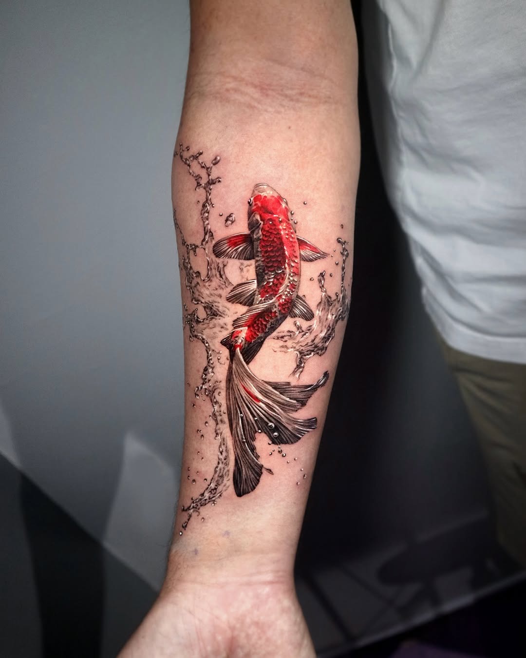 This tattoo features a striking red koi fish gliding through dynamic water splashes.
