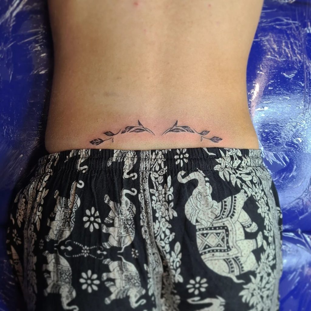 A minimalistic yet beautiful tattoo showing delicate vines with soft leaf detailing adorns the lower back.