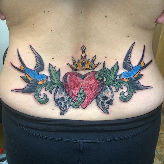 This colorful tattoo stands out with its red heart, crowned by a golden crown and flanked by swallows and skulls.