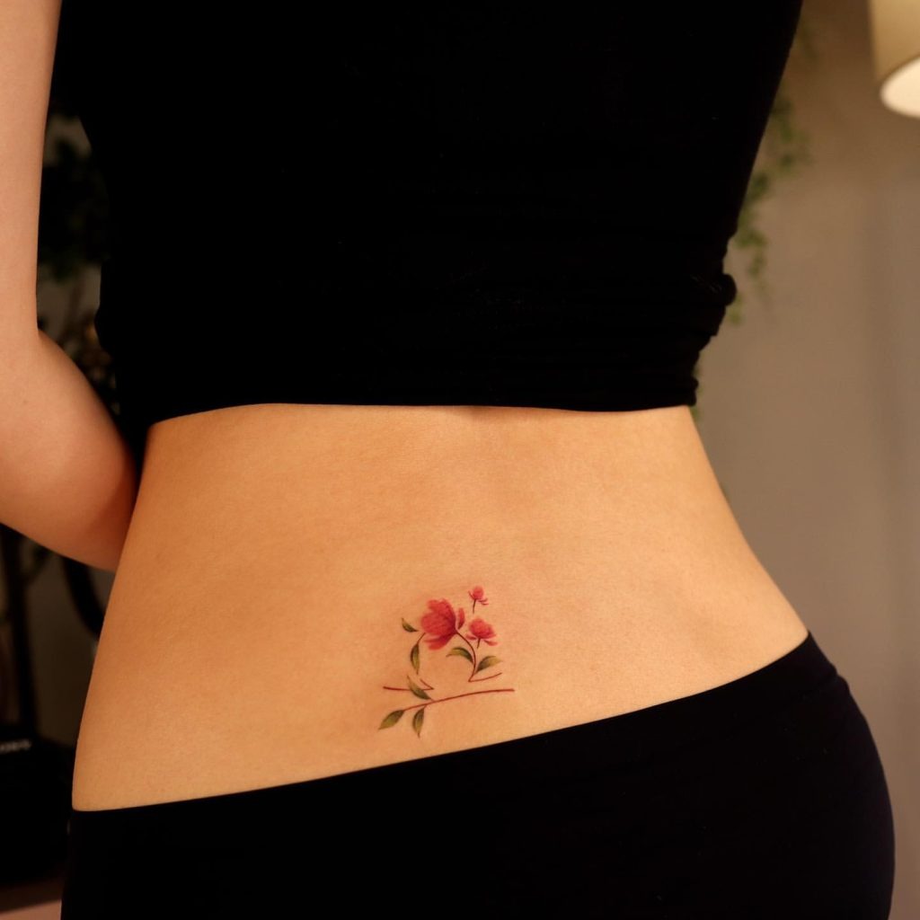 This tattoo presents a small, beautiful floral design with pink blooms and subtle green leaves.