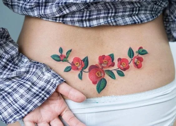 A burst of color adorns this tattoo, with red flowers and lush green leaves spanning the lower back.