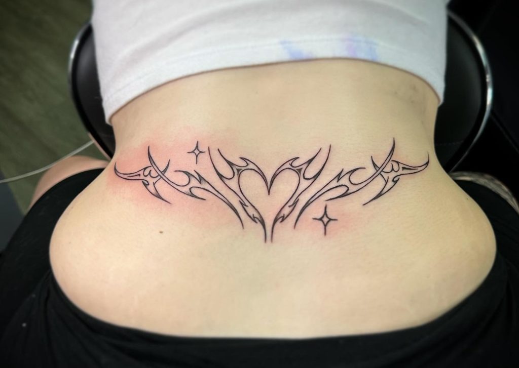 This delicate tattoo features a central heart encased within soft, flowing tribal lines and accompanied by tiny star accents.