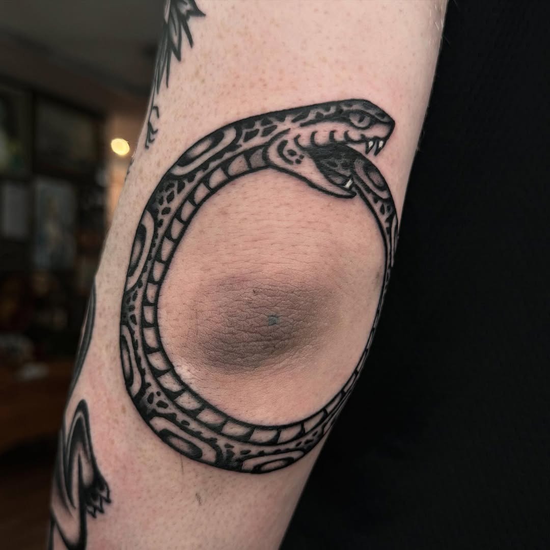 Bold ouroboros tattoo wrapping around elbow. Tattoo Design