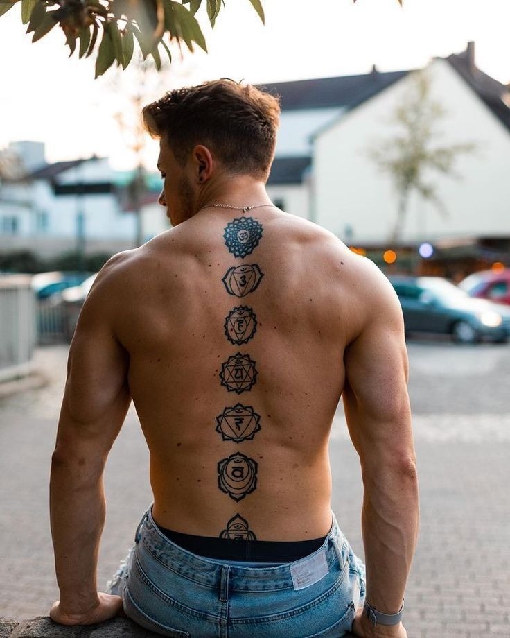 Each symbol in this vertical spine tattoo represents one of the seven chakras, moving from the base of the spine to the crown.
