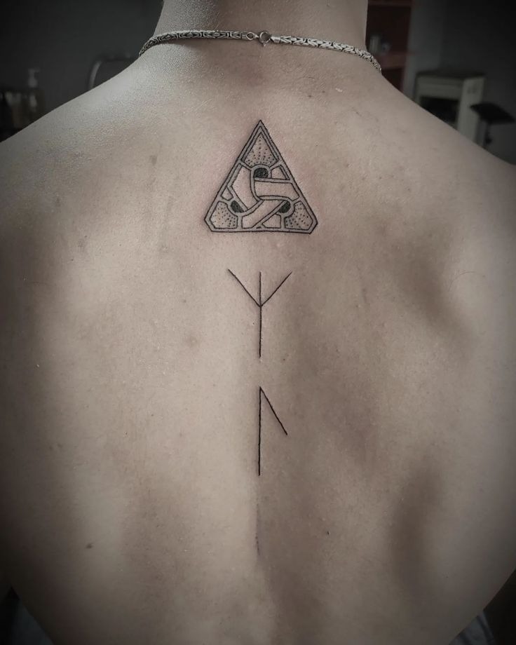 Minimal and fine line, this spine tattoo features a stylized Viking knotwork triangle paired with simple runes flowing downward.