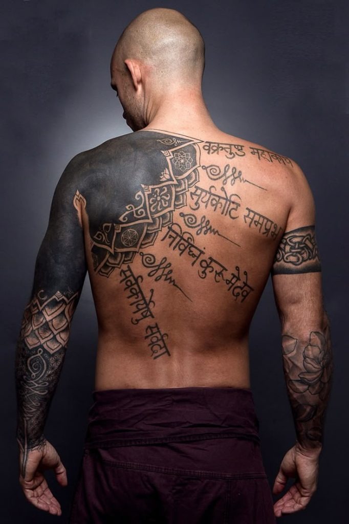 Bold, reverent, and deeply spiritual, this sweeping tattoo draws from traditional Indian Sanskrit in a beautifully scripted text style that flows diagonally across the back and spine.