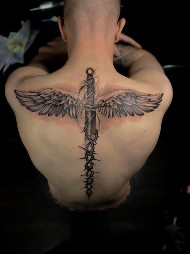 A vertical sword divides the back, sprouting angelic wings from its hilt and entwined with thorny vines, this design is equal parts sacred and savage.