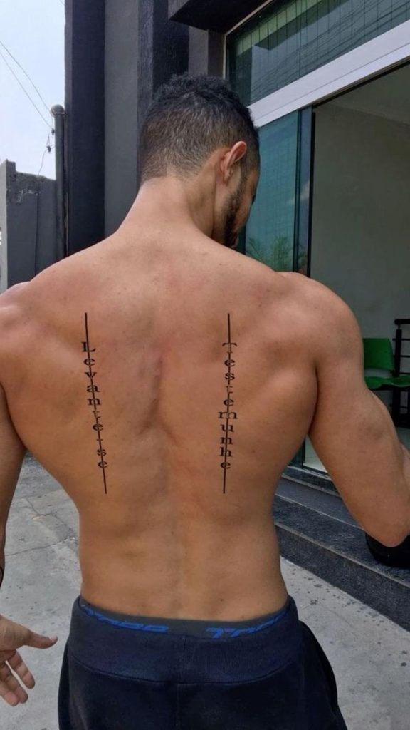 This vertical text tattoo pairs clean symmetry with meaningful quotes, one on each side of the spine.