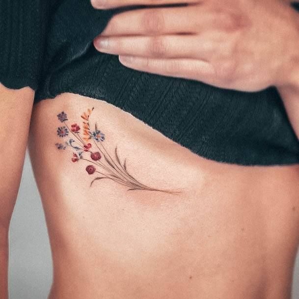 Tiny Wildflower Bouquet on the Ribcage, a tattoo design rendered in delicate fine-line.