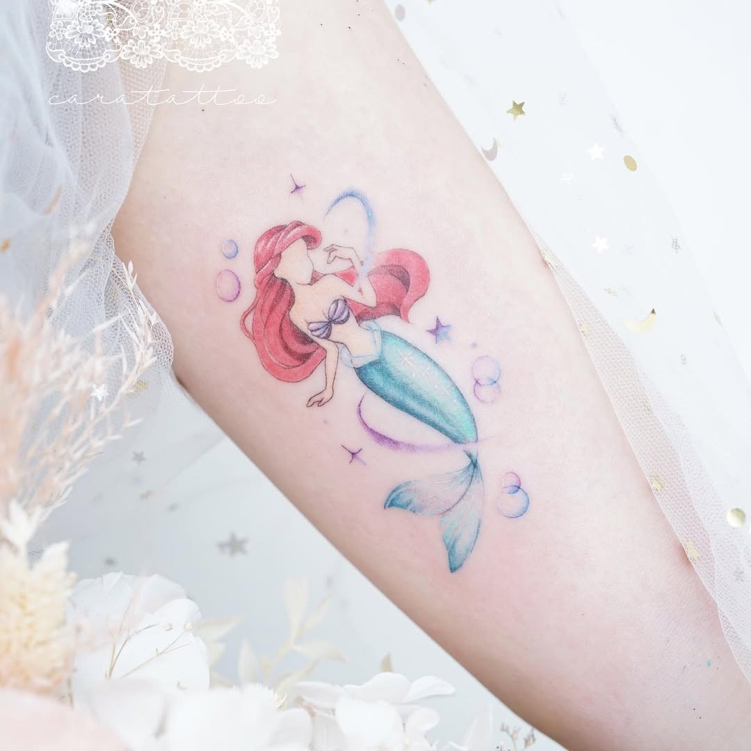This enchanting tattoo features Ariel, the beloved mermaid princess, gracefully swimming through a wave of bubbles.