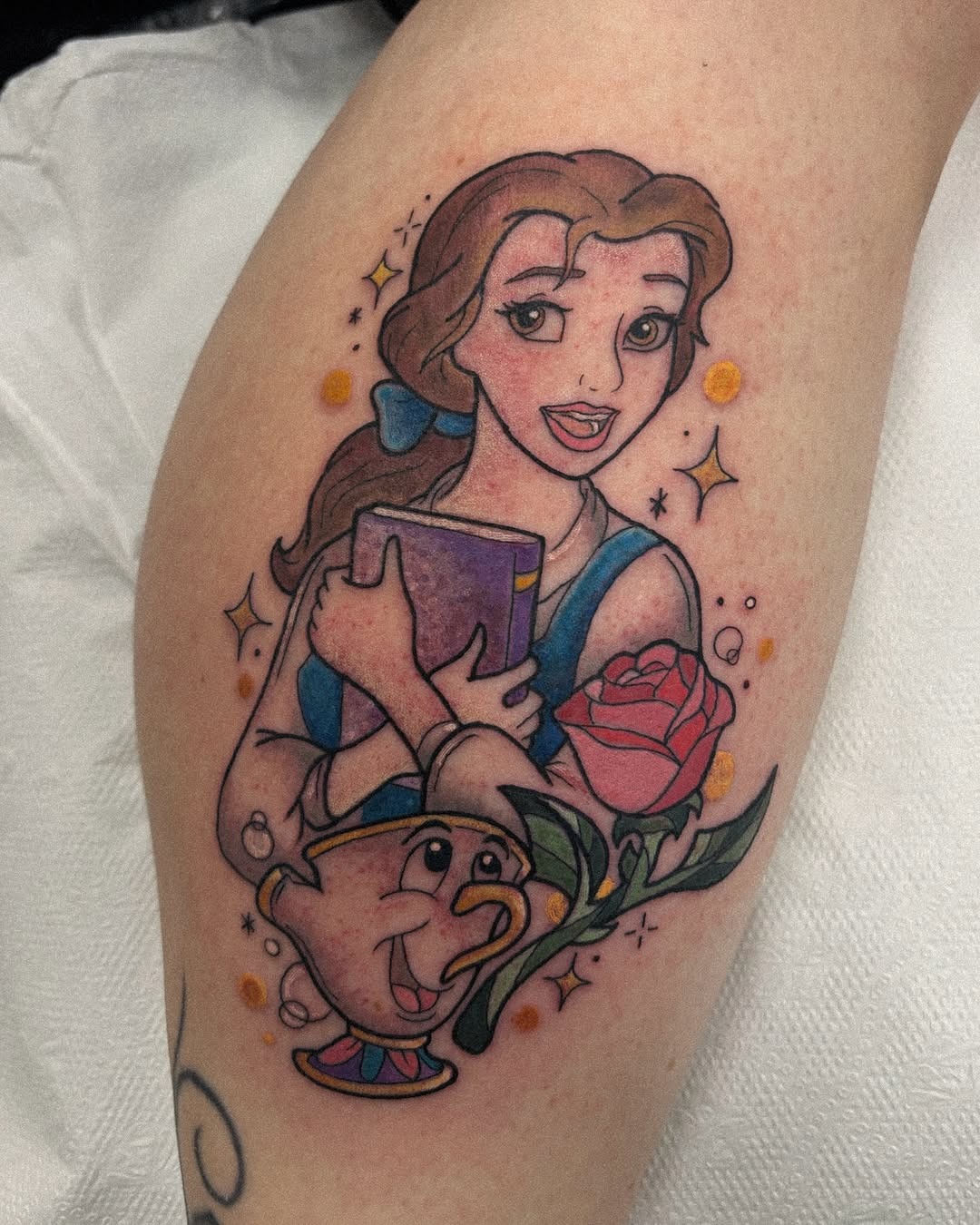 This tattoo beautifully captures Belle from 'Beauty and the Beast' surrounded by her beloved book and a rose.