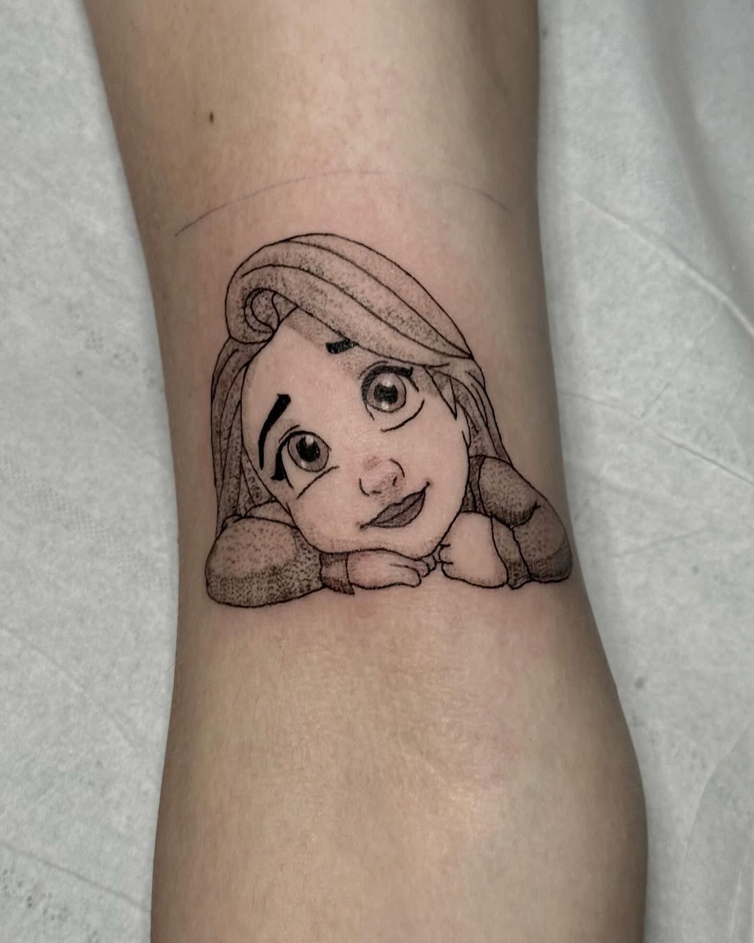This tattoo features Rapunzel resting her chin on her hands, showing her playful look.