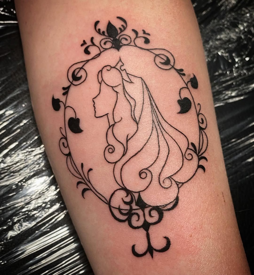 This tattoo features a delicate silhouette of a Disney princess, framed by ornate swirls and patterns.
