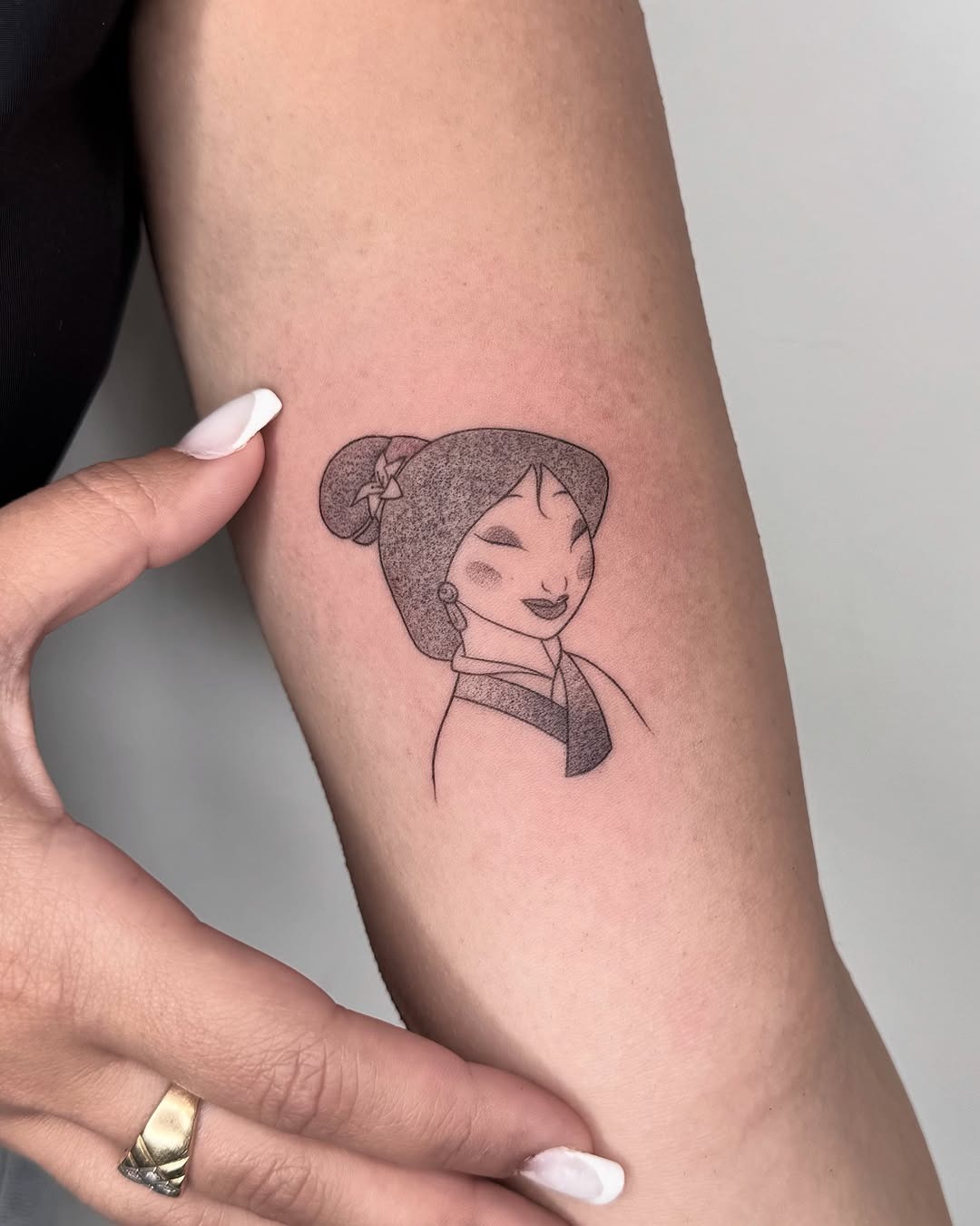 This minimalistic tattoo features Mulan with a confident expression, capturing her strong spirit.