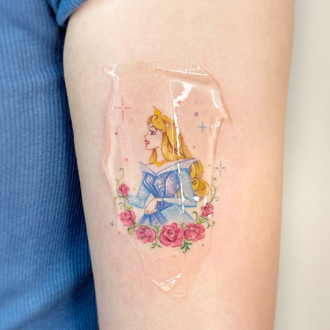 This tattoo features Princess Aurora from Disney's 'Sleeping Beauty' surrounded by delicate flowers.