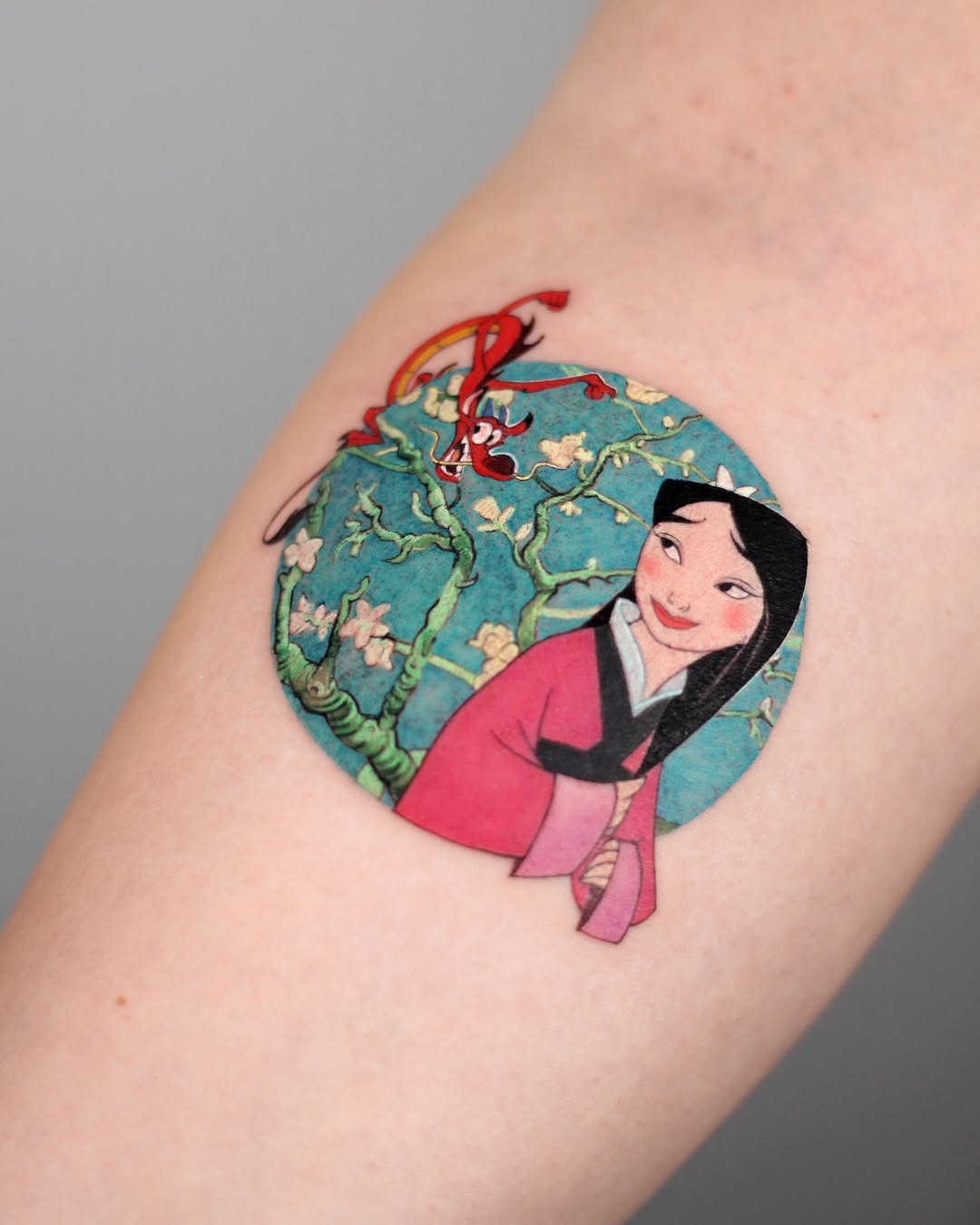 This tattoo features Mulan and Mushu surrounded by cherry blossoms.