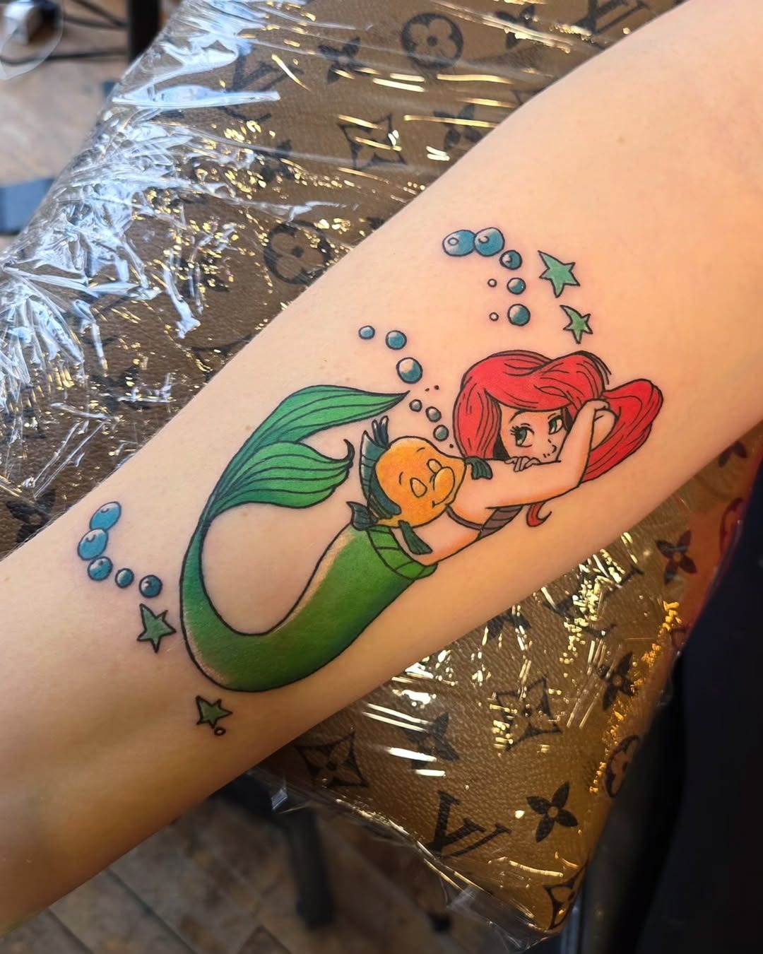 This colorful tattoo showcases Ariel, surrounded by playful bubbles and her best friend Flounder.
