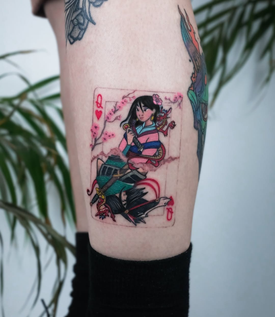 This tattoo showcases Mulan illustrated as a playing card queen, exuding strength and femininity.