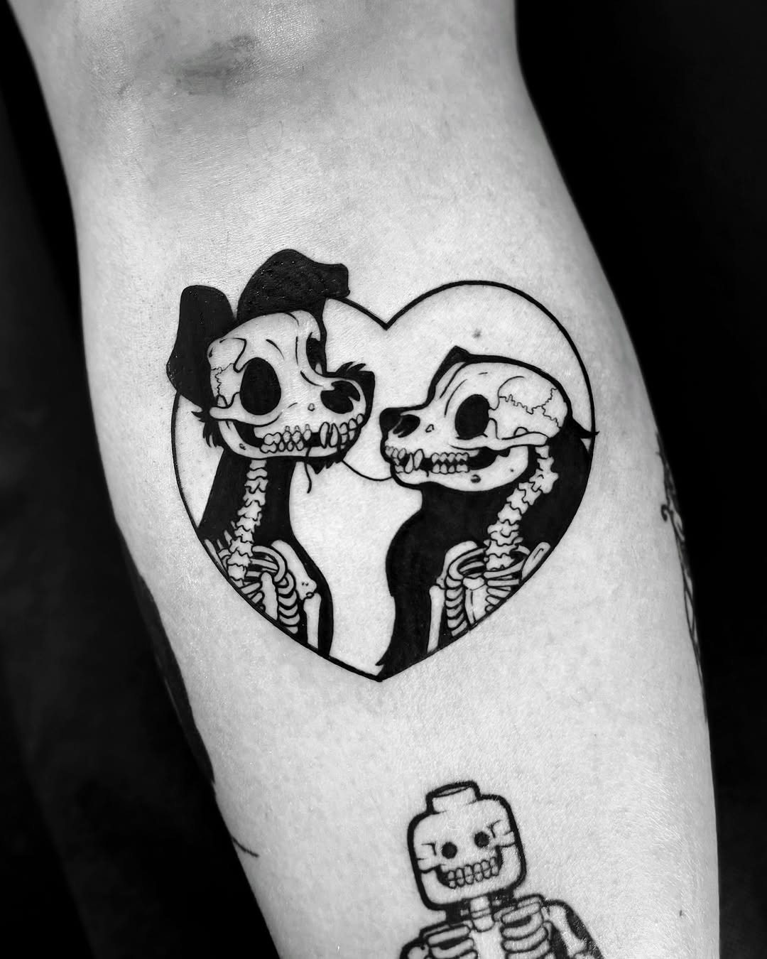 This tattoo features two Disney-inspired skeletons sweetly embracing within a heart.