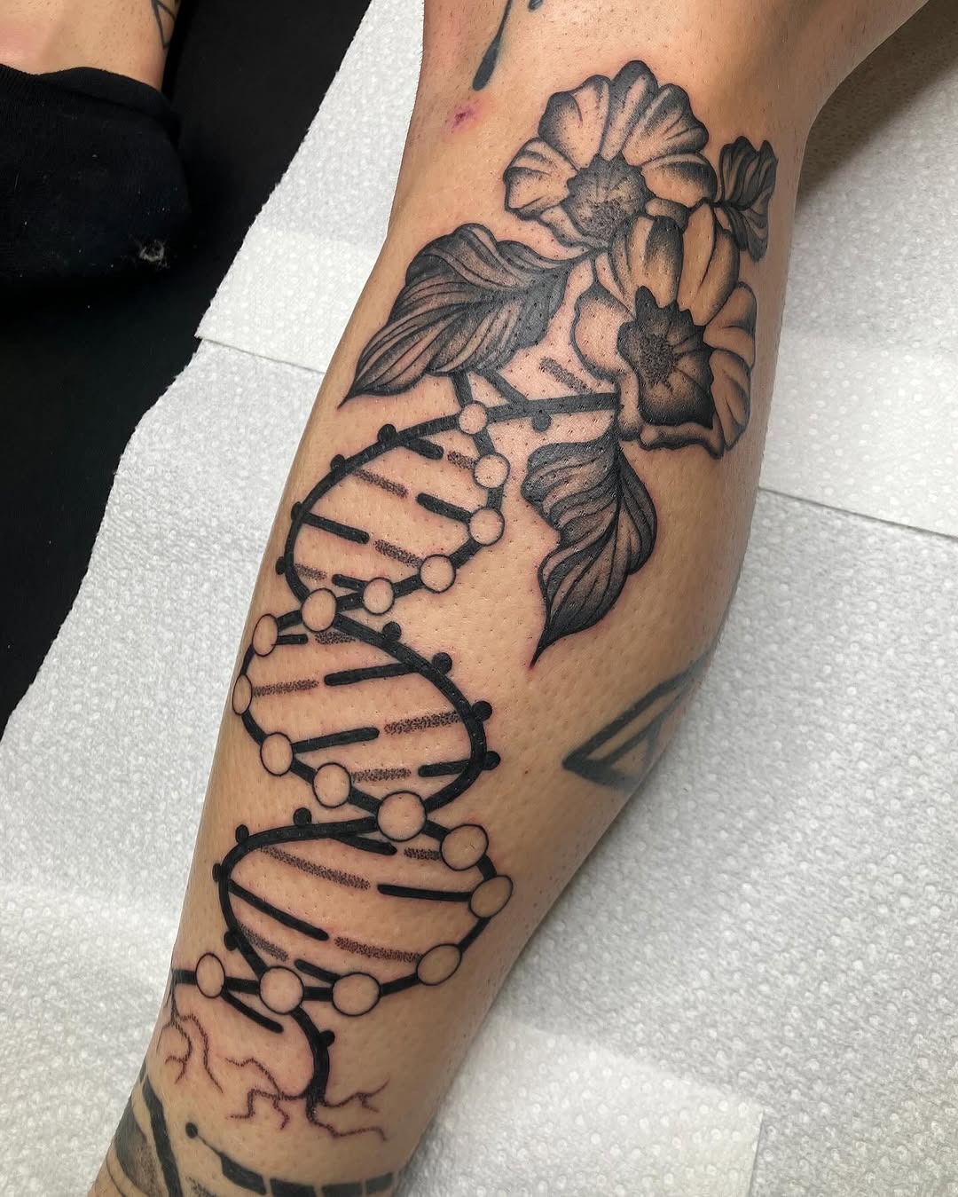 This tattoo features a stunning DNA helix intertwined with blossoming flowers.