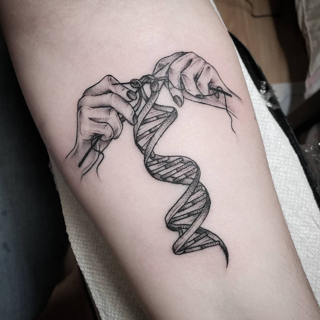 This tattoo beautifully showcases hands delicately stitching a DNA strand.