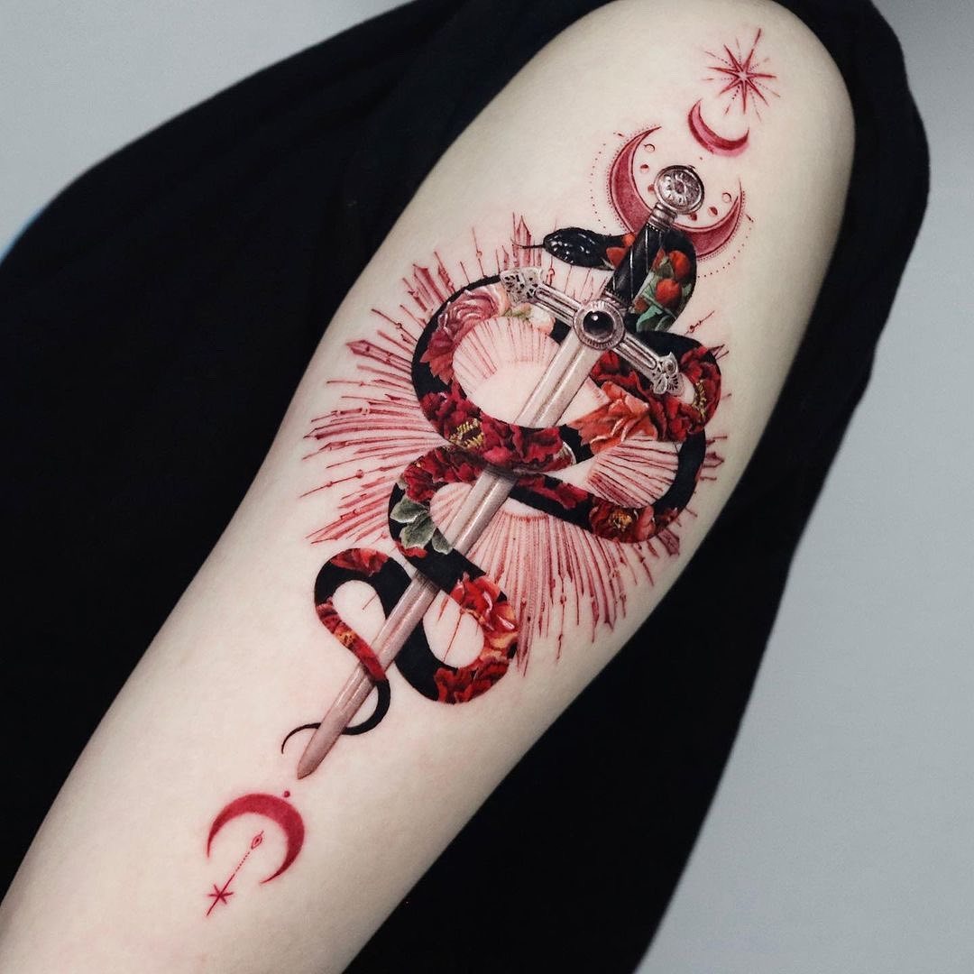 This tattoo features a striking design of a snake intertwined with a sword, surrounded by red roses.