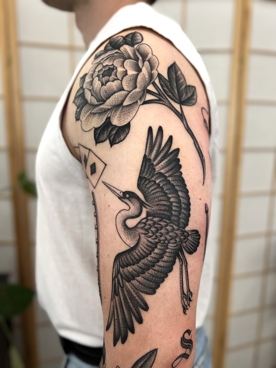 This striking tattoo features a crane elegantly soaring beside a detailed peony flower.