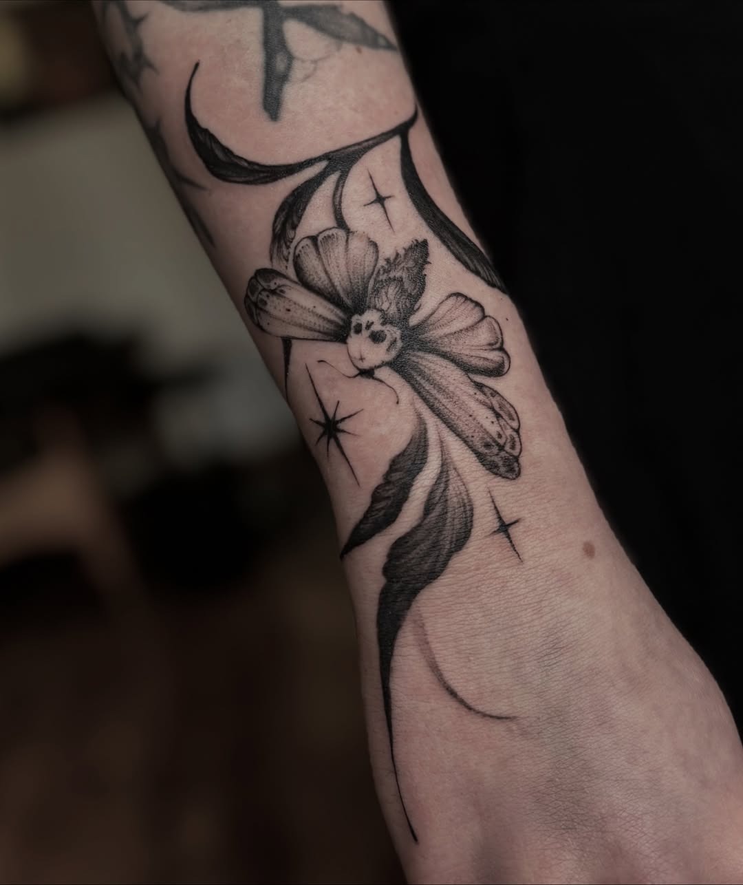 This stunning dotwork tattoo features a beautifully detailed flower design, intertwined with elegant lines and star motifs.