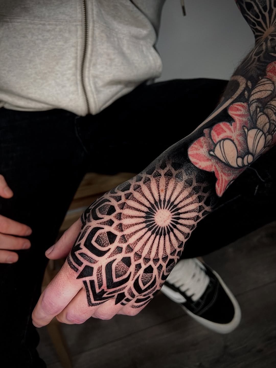 This striking tattoo features intricate dotwork on the hand that combines geometric elements with floral designs.