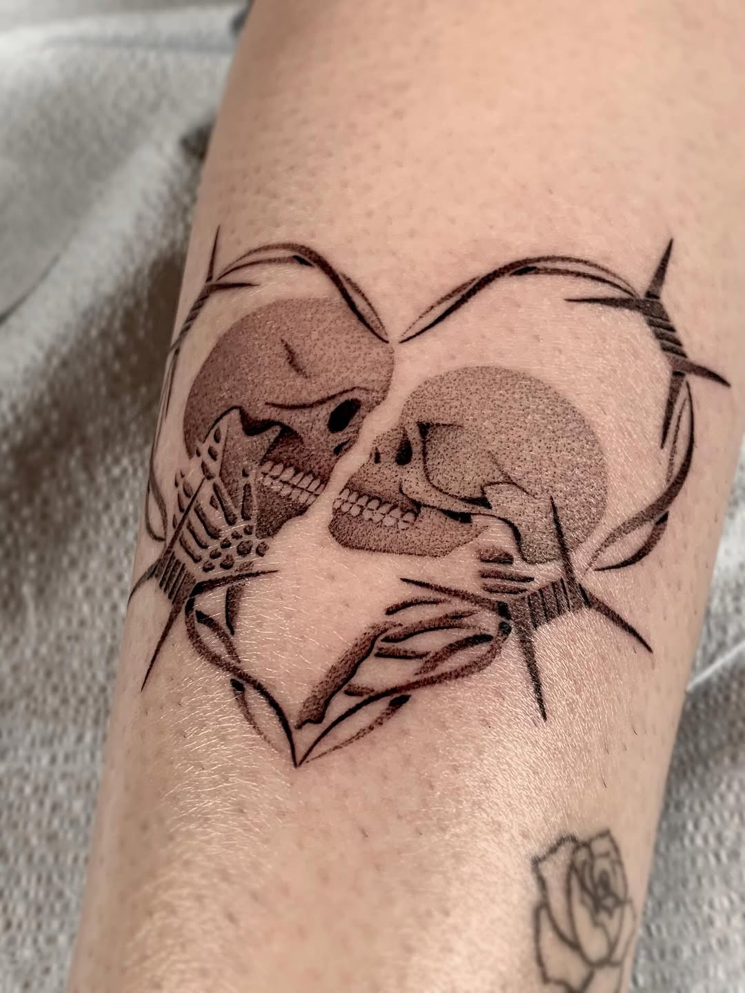 This striking dotwork tattoo features two skulls intertwined within a heart shape, creating a unique blend of love and mortality.