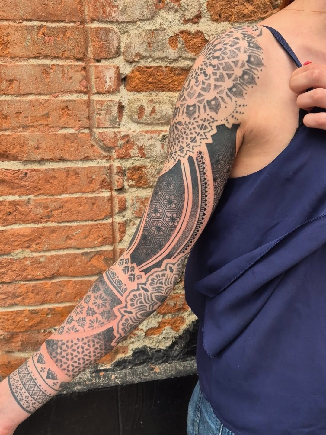 This stunning dotwork tattoo features a blend of geometric patterns and floral elements, creating a beautiful ornate effect on the wearer's arm.